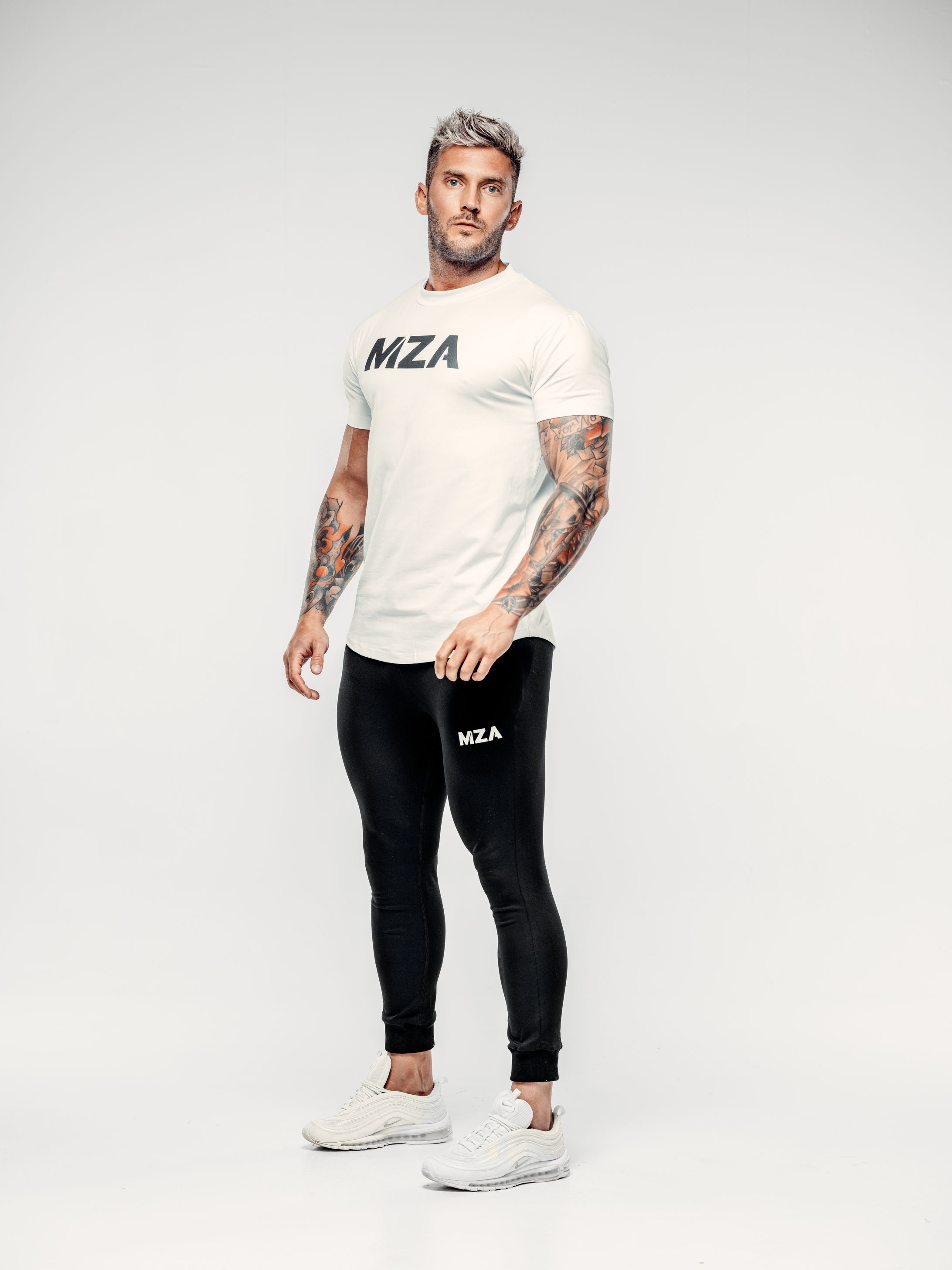 Shane is stood at a 45 degree angle wearing the new standard long line t-shirt in white with the new standard joggers in black
