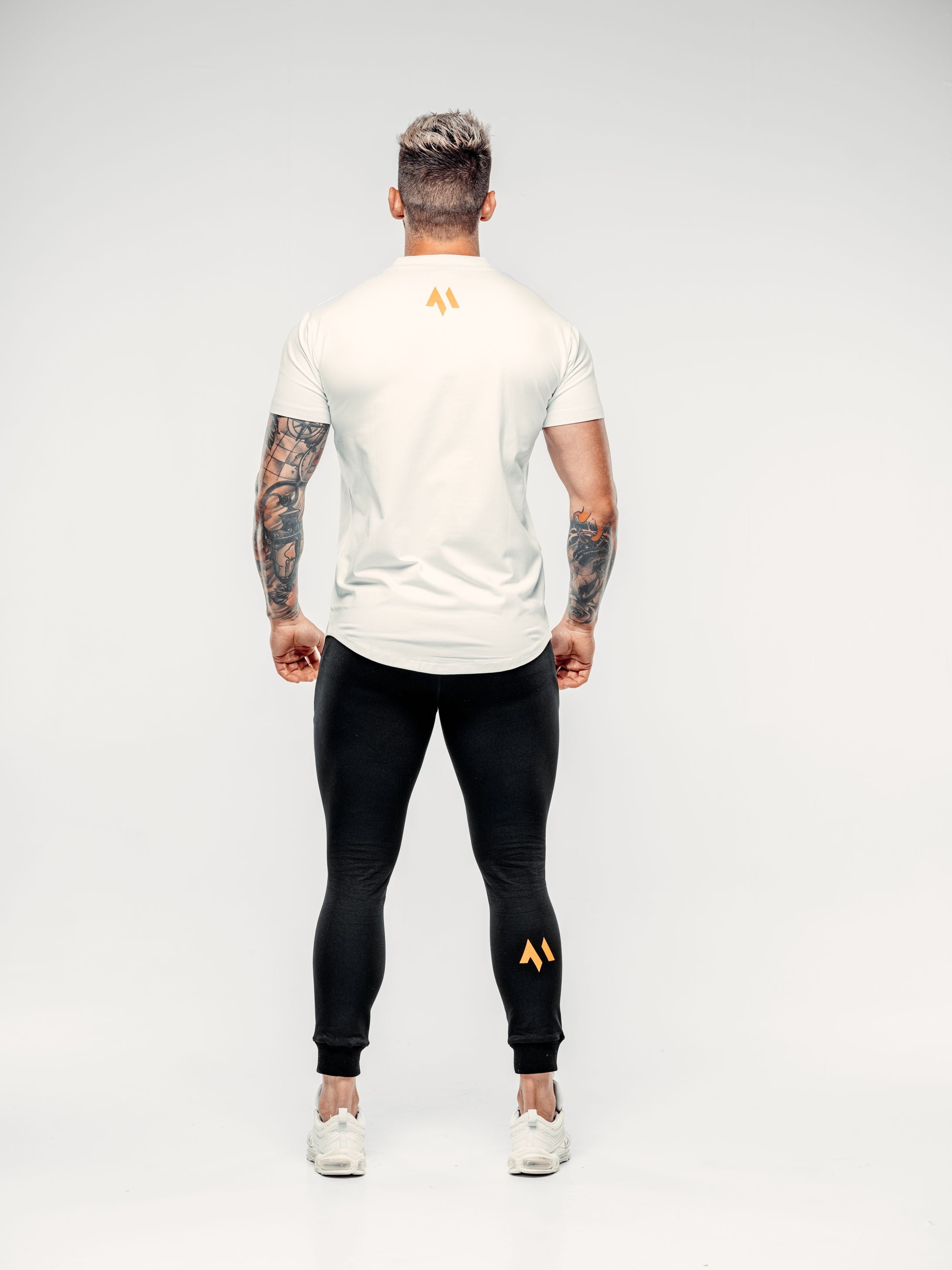 This is a rear view of Shane wearing the new standard long line t-shirt in white and the new standard joggers in black.  It showcases the emblem in orange on the t-shirt and trousers