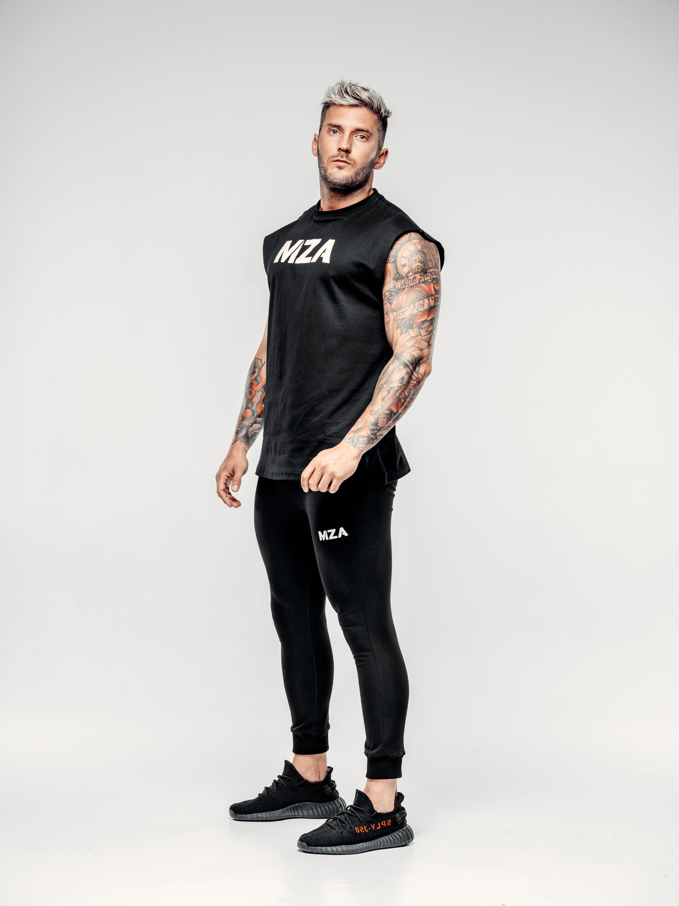 This is a full body shot of Shane stood at a 45 degree angle wearing the new standard vest in black paired with the new standard joggers in black