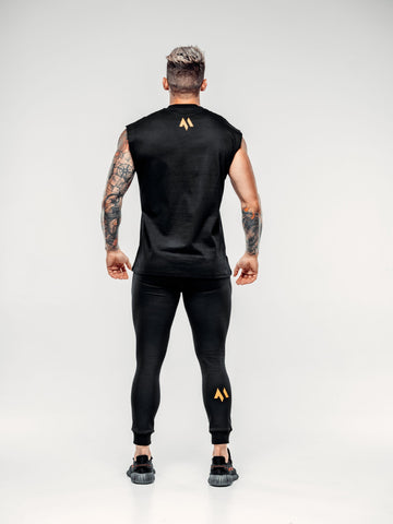This is a full body rear view shot of Shane wearing the new standard vest black paired with the new standard joggers in black.  It showcases the M emblem in signature orange underneath the neck and on his right calf