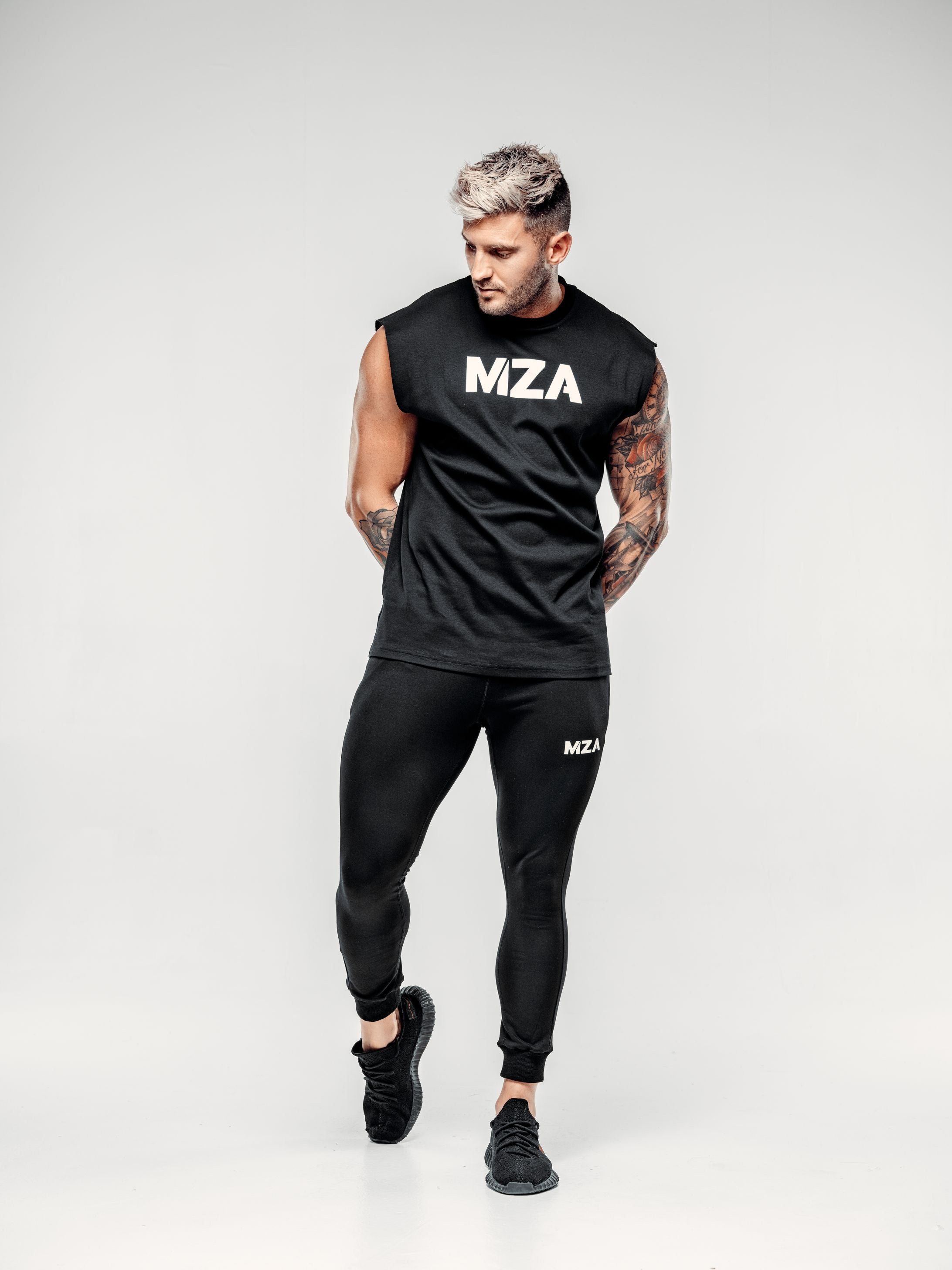 This is a full body shot of Shane looking down and to the right mid step wearing the new standard vest in black paired with the new standard joggers in black