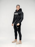 This is a full body shot of Shane at a 45 degree angle looking to the side wearing the new standard hoodie in black.  This features the MZA logo in white in the middle of his chest.  Shane is also wearing the matching new standard joggers in black.