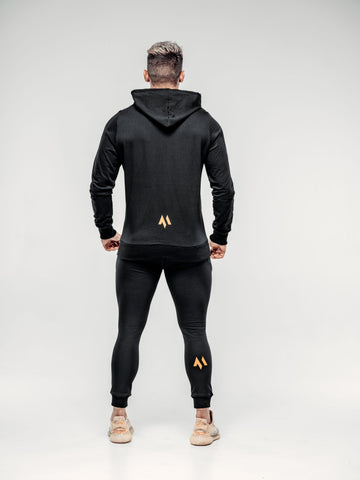 This is a rear view full body shot of Shane wearing the new standard hoodie in black.  It shows the M emblem in signature orange in the lower middle of the back as well as on the back of Shane's calf.