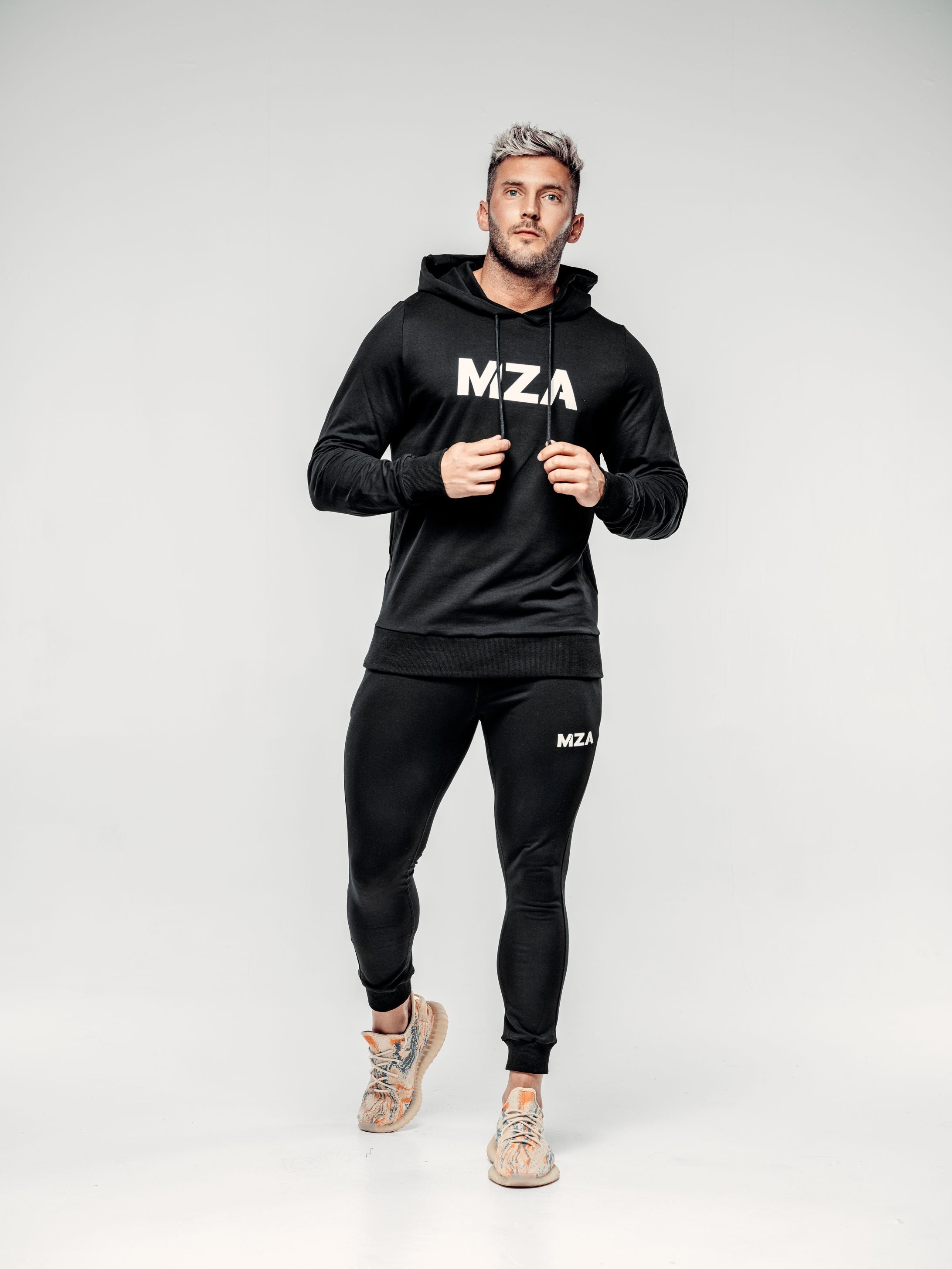 This is Shane wearing the new standard hoodie in black and the new standard joggers in black.  Matching hoodie and jogger combo.  Shane is taking a step forwards and is holding both strings of the hoodie