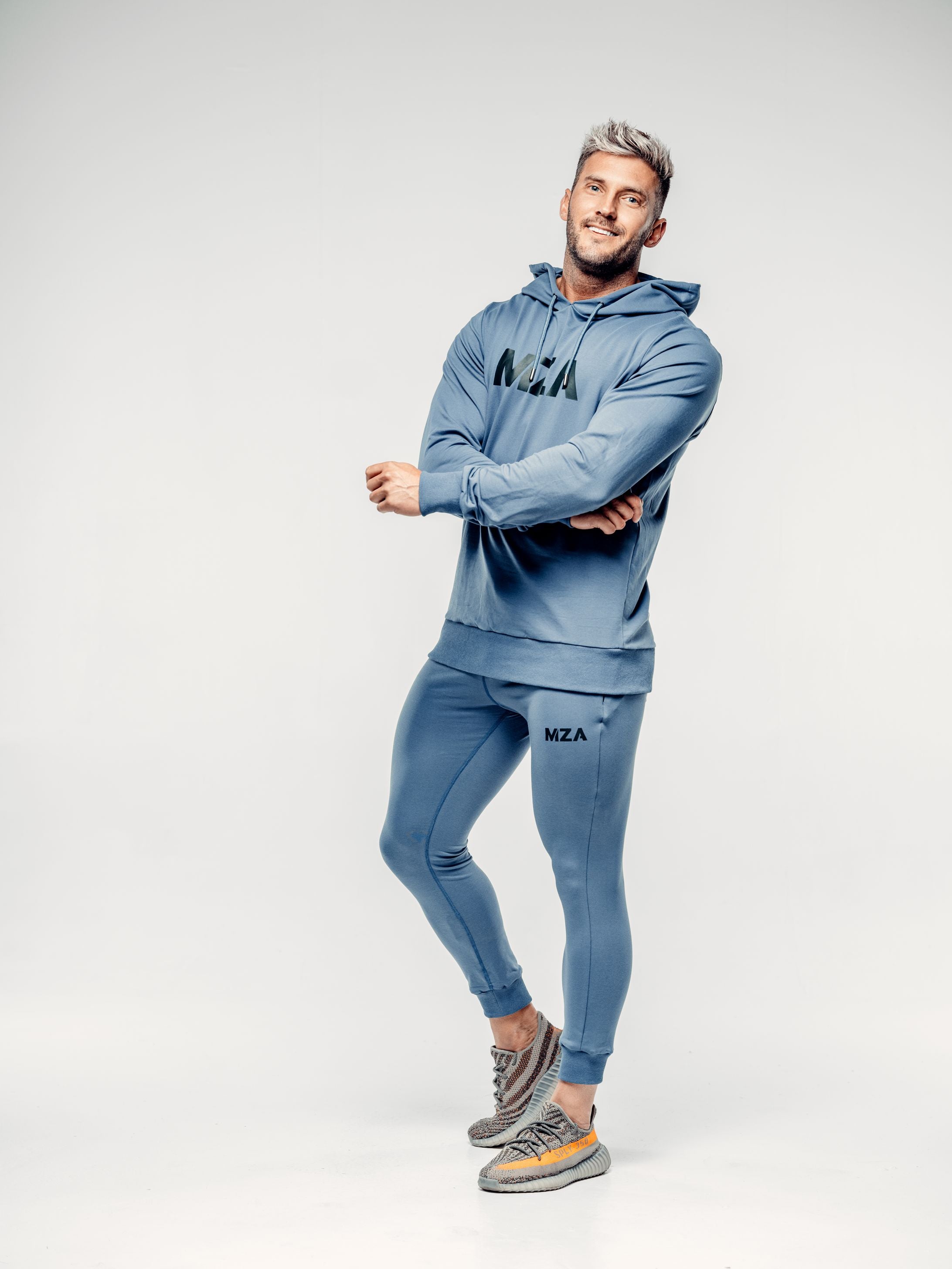 This is Shane wearing the New standard hoodie and new standard joggers combo in blue steel.  Shane has his arms crossed and is smiling.