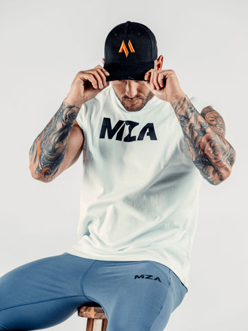 This is a front view of Shane wearing the new standard 3d distressed 5 panel in black which features the orange M emblem.  Shane is looking down with the peak covering his eyes.  Shane is holding on to the peak as if pulling it down.  He is also wearing the new standard vest in white with the MZA text logo on the chest and the new standard joggers in blue