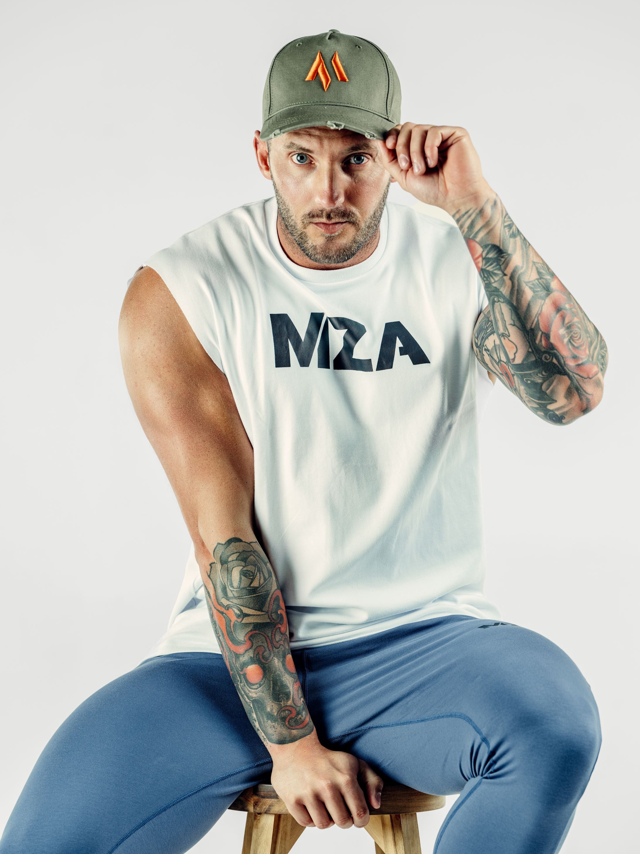 This is a front view of Shane wearing the new standard 3d distressed 5 panel in khaki.  Shane is holding the peak with one hand and his chair with the other.  He is also wearing the new standard vest in white and new standard joggers in blue