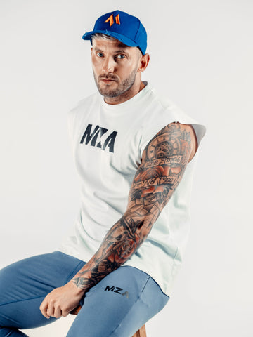 This is Shane sat on a stool facing the camera wearing the black new standard 3d distressed 5 panel electric blue with an orange emblem. He is wearing the new standard vest in white and the new standard joggers in blue