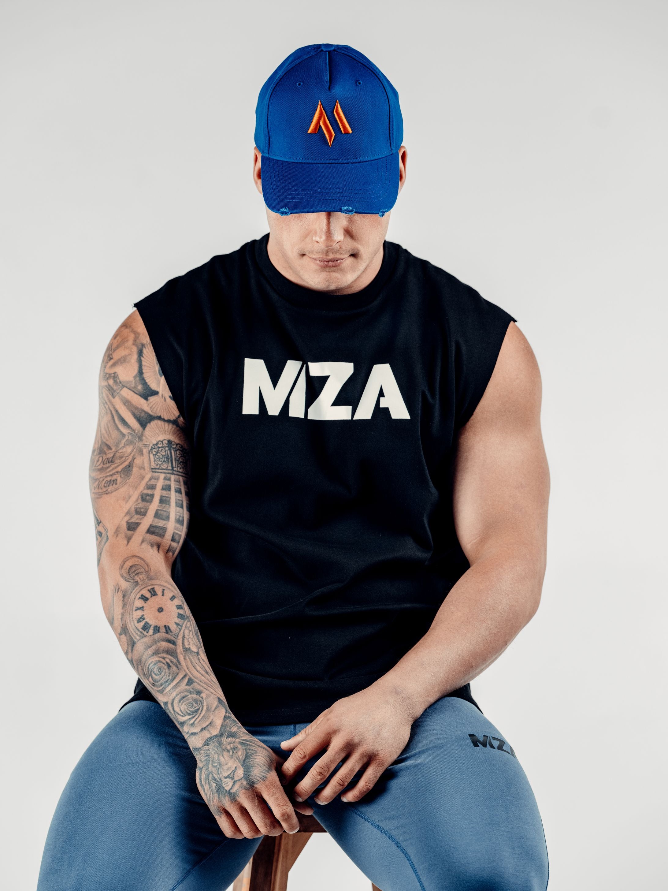 This is Lewis wearing the new standard 3d distressed 5 panel in electric blue.  It features the M emblem in orange.  Lewis is looking down with the peak covering his eyes and is also wearing the new standard vest in black and new standard joggers in blue