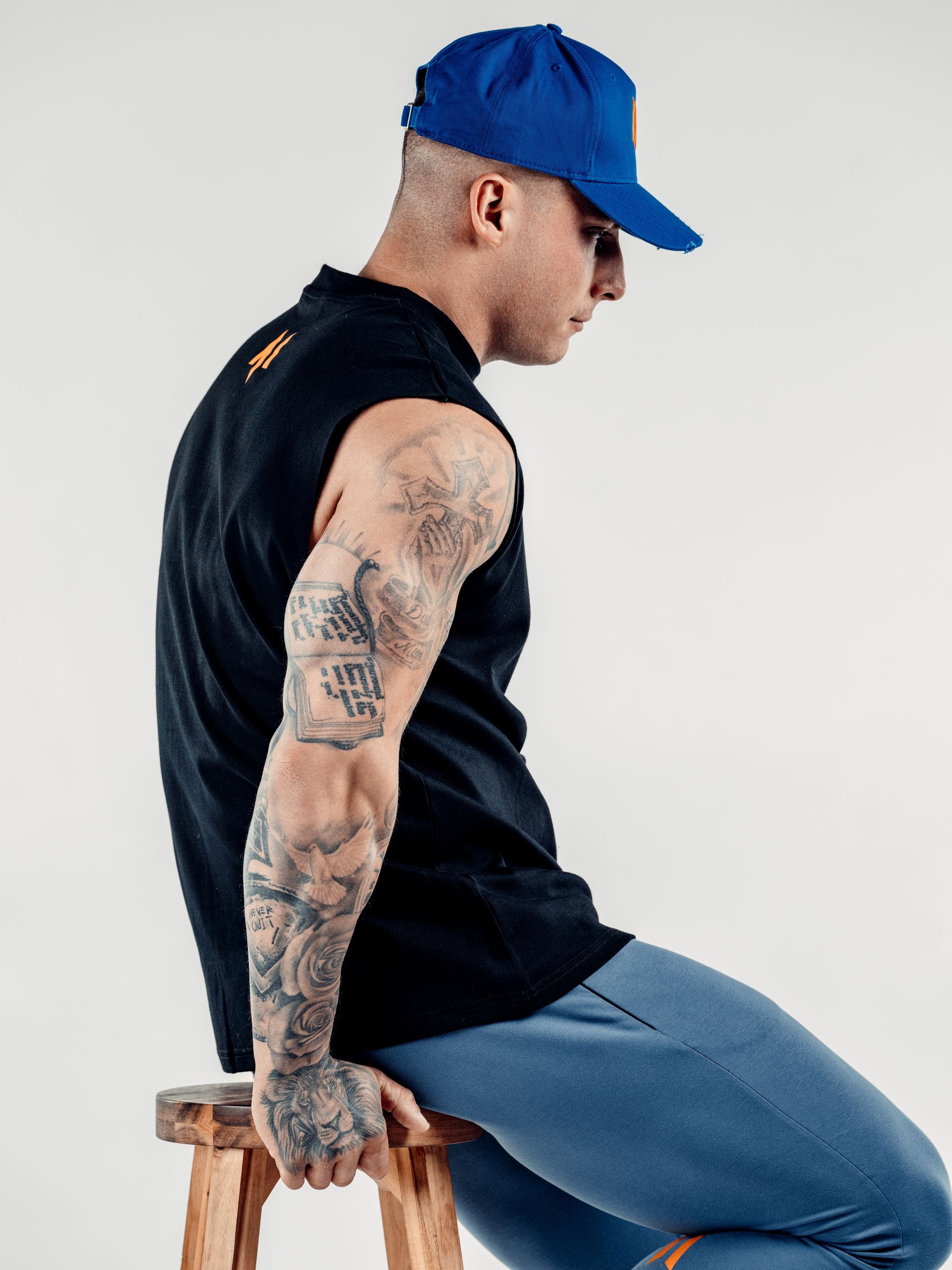 This is a rear sideview of Lewis wearing the new standard 3d distressed 5 panel in electric blue. It shows off the strap, buckle and how the peak fits from a side profile. Lewis is also wearing the new standard vest in black featuring the M emblem at the top of his back.
