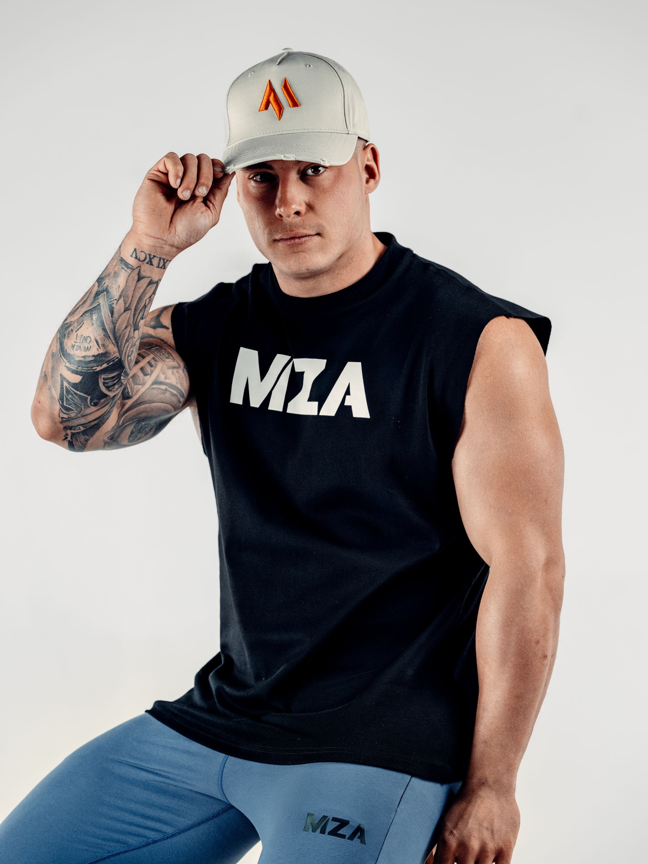 This is a front on view of Lewis wearing the new standard 3d distressed 5 panel in stone. Lewis is also wearing the new standard vest in black and new standard joggers in blue.  Lewis is holding the peak of the hat
